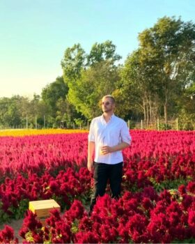 Casey Pownall stands in a field of red flowers, on a sunny day.